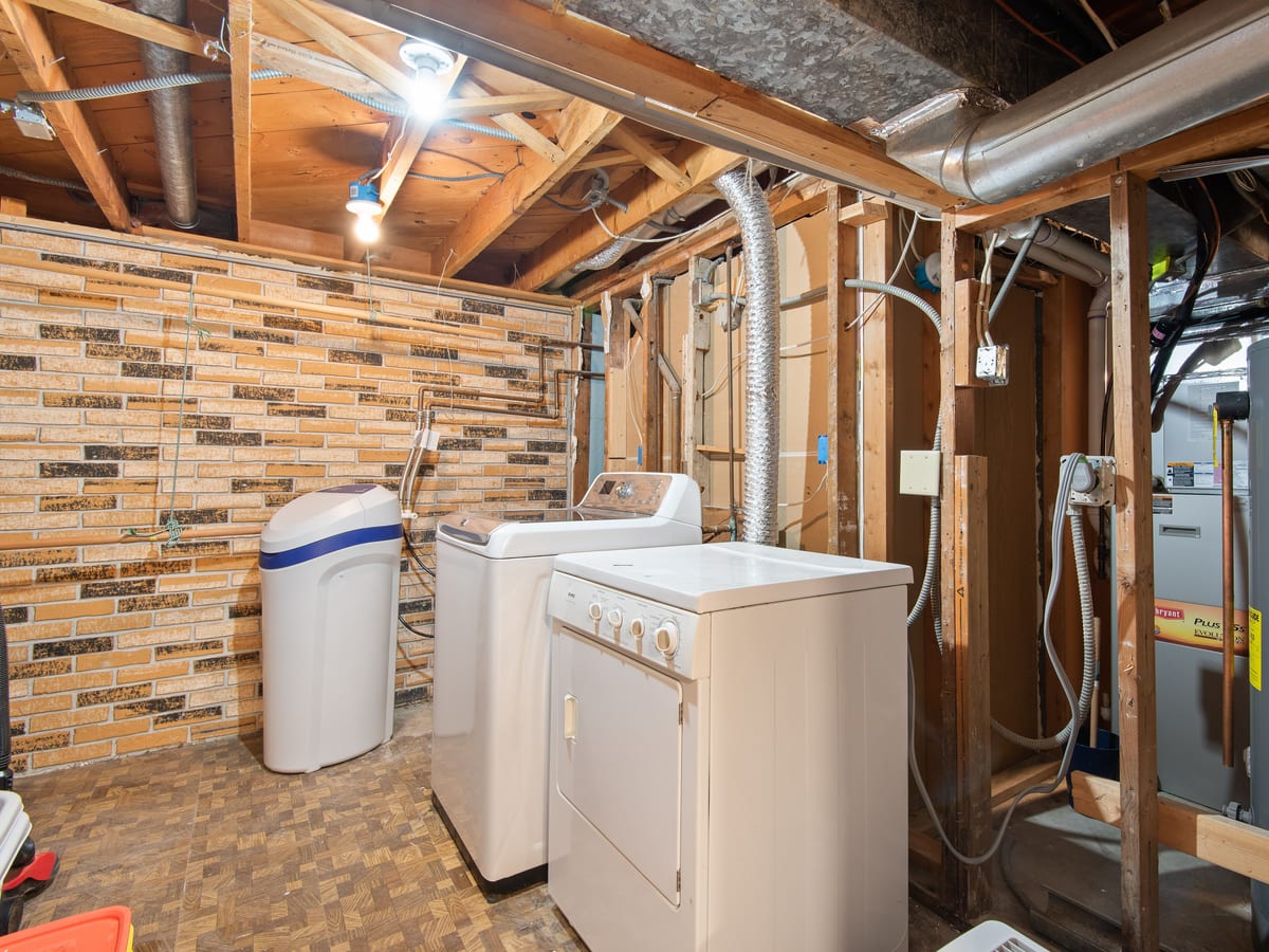 Spacious basement laundry room featuring modern appliances and exposed brickwork.